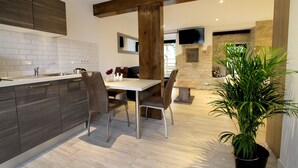 A modern kitchen with dark cabinetry, a white countertop, and a dining area with a table and chairs. - Logis/Jacuzzi Studio **** La chute 40m² from 1 to 2 pers freiburg, basel, colmar  (Baldersheim)
