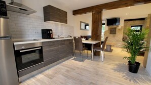 A modern kitchen with a built-in oven, a microwave, and a stainless steel refrigerator. There is a dining area with a table and chairs. - Logis/Jacuzzi Studio **** La chute 40m² from 1 to 2 pers freiburg, basel, colmar  (Baldersheim)