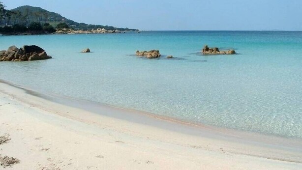 Ein Strand mit klarem türkisblauem Wasser, Sandstrand und vereinzelten Felsen.
