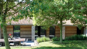 A building with a tiled roof, brick walls, and a covered patio area with a table and chairs. - A Cocoon for 2 People With a Beautiful View of the Valley Tournai (Beclers)