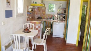 Uma cozinha compacta com área de refeições, cadeiras brancas, uma mesa pequena e uma máquina de lavar louça branca.