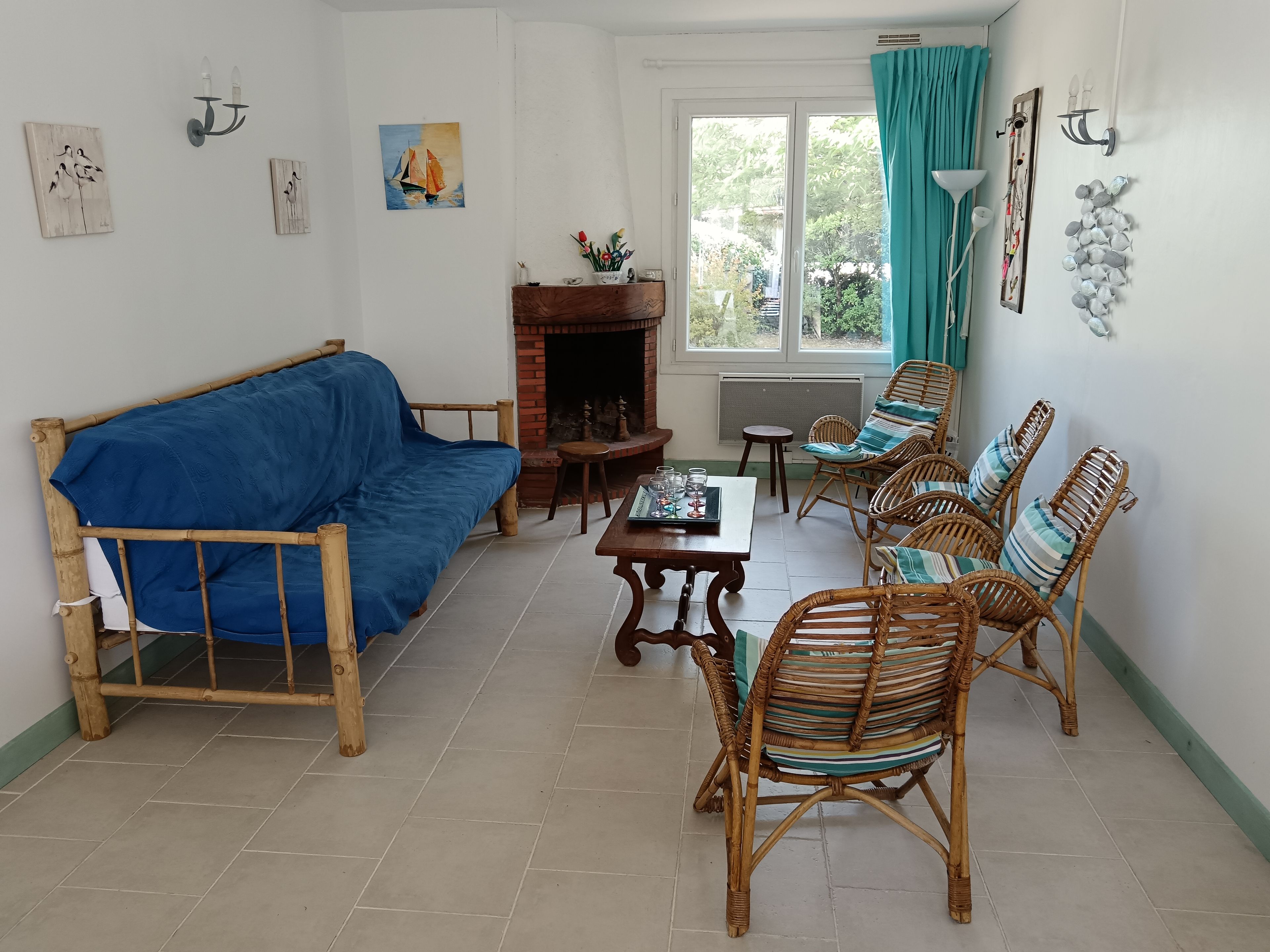 Un salon comprenant un canapé, des fauteuils en osier, une table et une cheminée.
