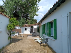 A courtyard with a white building, green shutters, and outdoor seating. - Ile d'Oleron (17) House / Villa 8/9 pers, 500 m from the beach of Les Sables Vignier (Saint-Georges-D'oléron)
