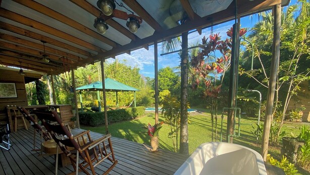 A wooden deck with a hot tub, rocking chairs, and a view of a garden and pool.