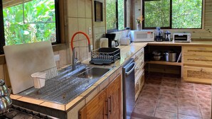 A kitchen with wooden cabinets, a sink, a microwave, a toaster, and a window with a view of greenery.