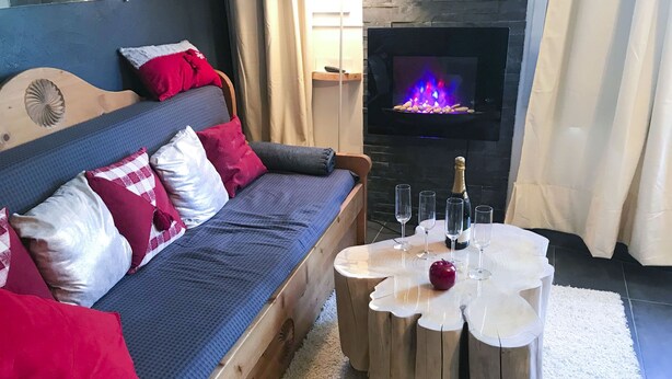Una sala de estar acogedora con un sofá de madera, una chimenea y una mesa de centro redonda de madera con vasos y una botella.