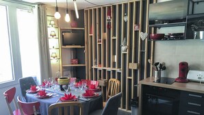 Un comedor con una mesa dispuesta para cuatro, una cocina con electrodomésticos modernos y una pared decorativa con diversos adornos.