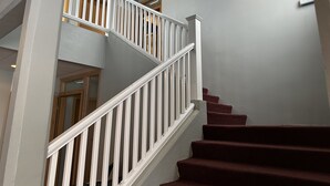 A staircase with white railings and red carpeted steps, leading to an upper floor. - Hotel Kanslarinn (Rangárþing ytra)