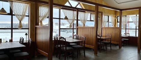 A restaurant with wooden paneled walls, large windows with lace curtains, and a view of a snowy landscape.