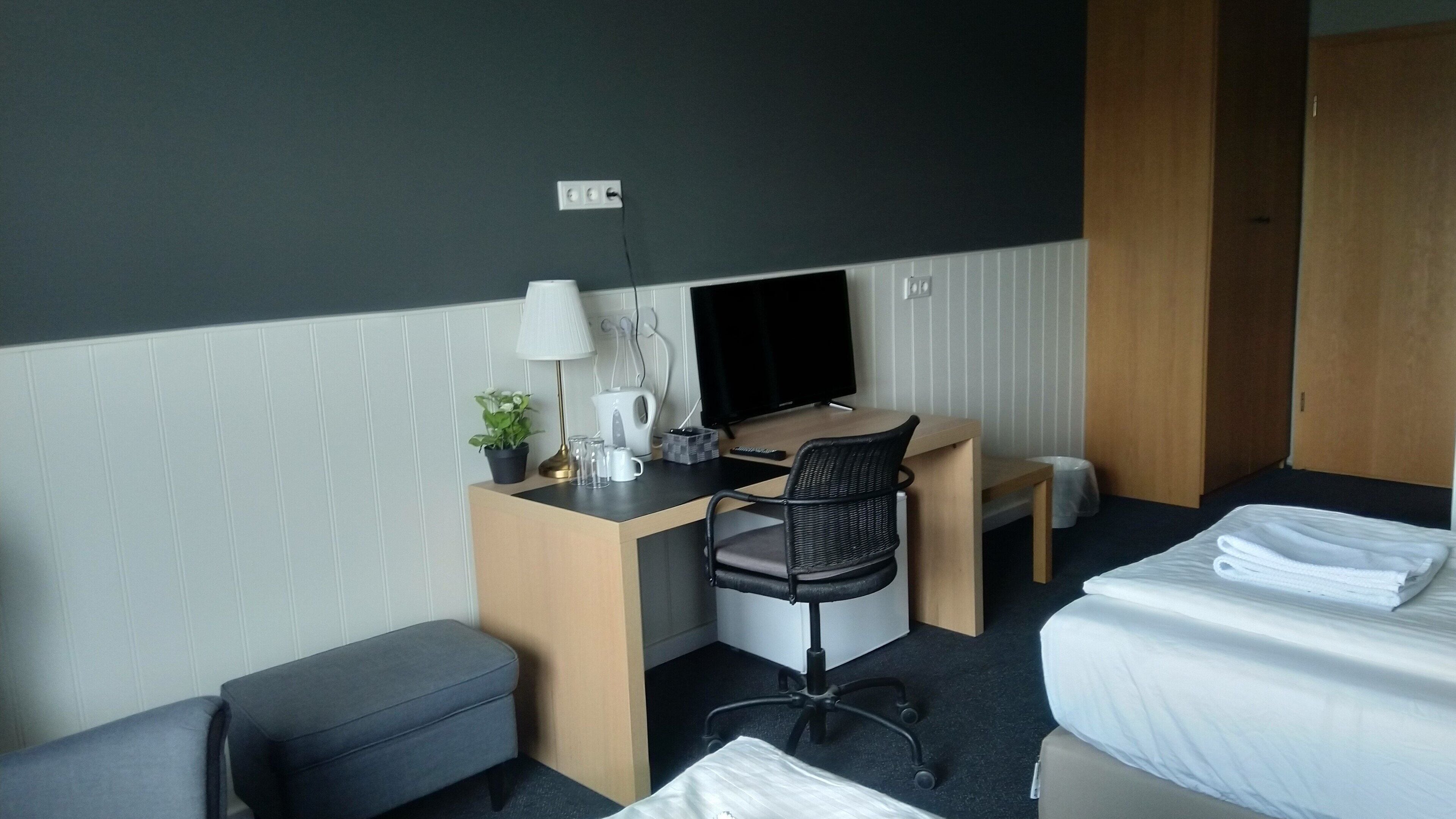 Une chambre d’hôtel comprenant un lit, un bureau avec un ordinateur, une chaise, une petite table et une table de chevet avec une lampe.
