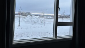 A window with a view of a snowy landscape, a pile of snow, and a building in the distance. - Hotel Kanslarinn (Rangárþing ytra)