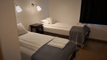 Una habitación con dos camas, cada una con una almohada y una manta. Hay dos lámparas fijadas a la pared.