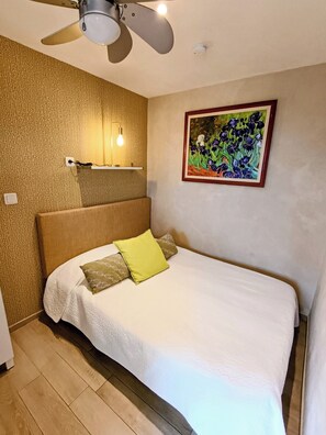 Une chambre à coucher avec un lit, un ventilateur de plafond, une lampe fixée au mur et un tableau encadré.