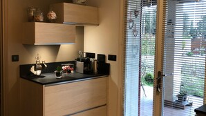 A modern kitchen with a black countertop, wooden cabinets, and a built-in oven. There is a window with blinds, a door, and a small outdoor area visible through the window. - Sun of the Hermitage. Villa with pool 6/8 persons, Family holidays (Carpentras)