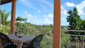 A balcony with a table and chairs, overlooking a lush green landscape and a clear blue sky. - Superb accommodation in a green location with private pool. (Sainte Anne)
