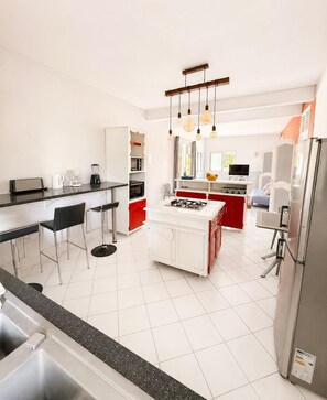 Une cuisine moderne dotée d’un îlot central, de tabourets de bar, d’une cuisinière encastrée et d’un réfrigérateur.