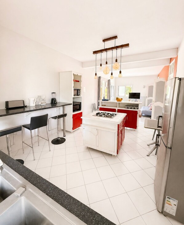 A modern kitchen with a central island, bar stools, a built-in stove, and a refrigerator.