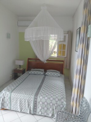 Une chambre à coucher comprenant un lit, une table de chevet, une lampe, une fenêtre avec des rideaux et un climatiseur fixé au mur.