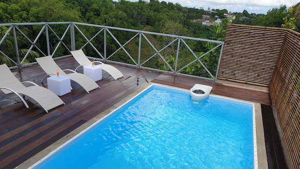 A swimming pool with a wooden deck, white lounge chairs, and a view of the surrounding greenery. - Superb accommodation in a green location with private pool. (Sainte Anne)