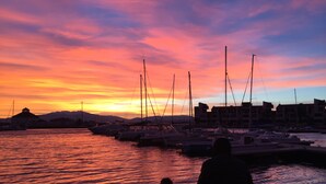 Een jachthaven in de zonsondergang, met aanmerende boten, een persoon zittend op een bankje en gebouwen op de achtergrond.
