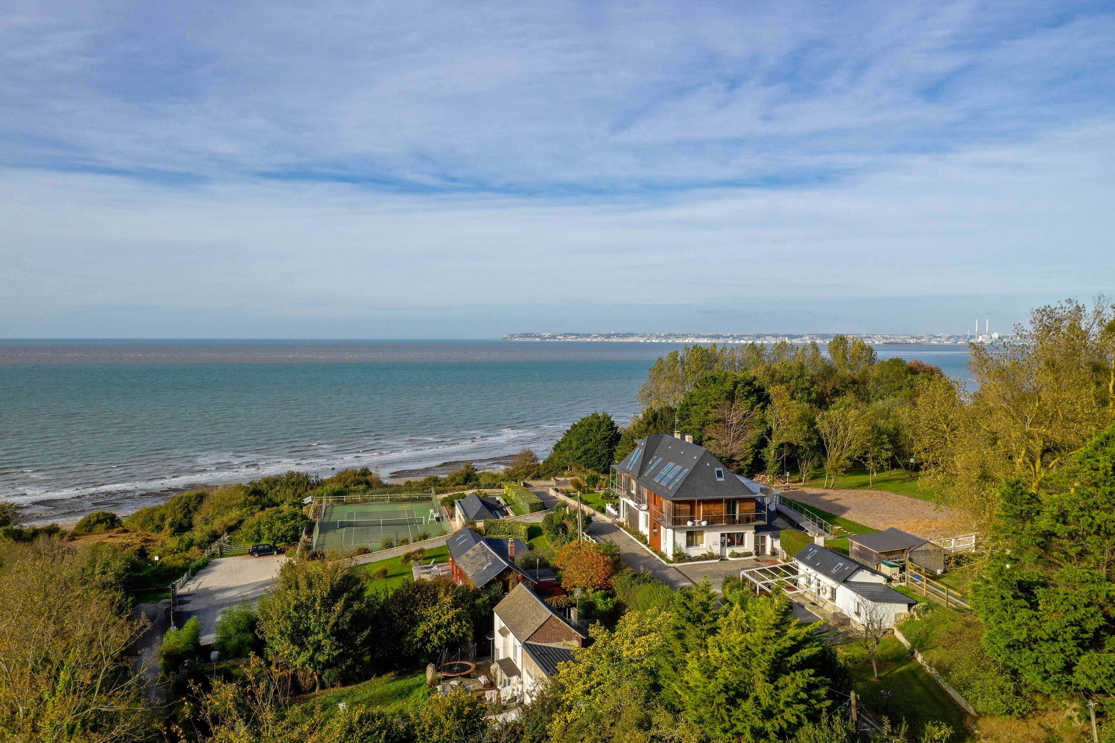 A coastal residential area with houses, a tennis court, and a view of the sea.