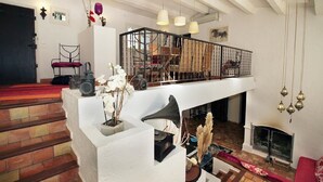 A spacious living area with a high ceiling, a staircase leading to a balcony, a fireplace, and a variety of decorative items including flowers and a vintage radio. - PROVENCAL MAS PISICINE JACUZZI CLIM 10 PEOPLE (JUAN LES PINS)