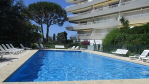 A rectangular swimming pool with clear blue water, surrounded by white lounge chairs and a stone-tiled deck.