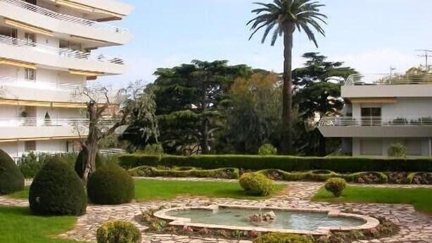 A courtyard with a fountain, neatly trimmed hedges, and a palm tree.