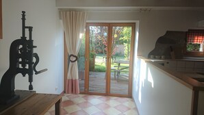 Une cuisine avec une table en bois, une porte-fenêtre coulissante donnant sur un patio et un four en pierre.