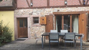 A wooden deck with a table and chairs, a stone wall, and a wooden door with a window.