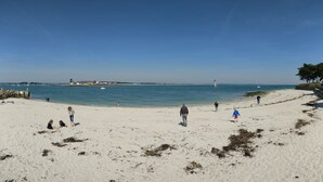 A sandy beach with people walking and playing, a lighthouse in the distance, and calm waters. - House Heart LOCTUDY - Close Sea and Beach on foot. (Loctudy)