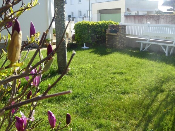 A well-maintained lawn with a white fence, a stone wall, and a bench.