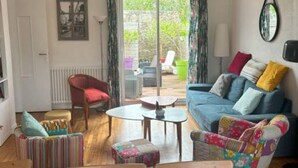 A spacious living room with a blue sofa, colorful chairs, a wooden dining table, and a large window with curtains. - House Heart LOCTUDY - Close Sea and Beach on foot. (Loctudy)