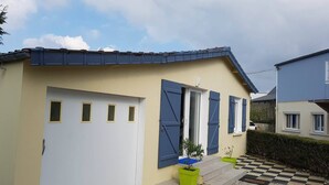 A two-story house with a garage, a small garden with potted plants, and a checkered pathway leading to the entrance. - 800M from the sea, renovated gite  (Agon-Coutainville)