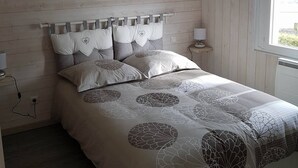 A bedroom with a wooden headboard, a bed with a leaf-patterned duvet, and a bedside table with a lamp. - 800M from the sea, renovated gite  (Agon-Coutainville)