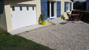 A single-story house with a white exterior and blue shutters, a front door, and a small patio with a table and chairs. - 800M from the sea, renovated gite  (Agon-Coutainville)