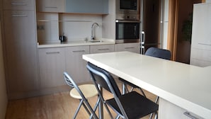 A modern kitchen with a large island, stainless steel appliances, and a dining area with foldable chairs.