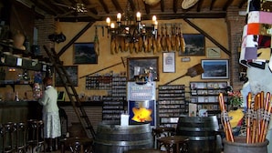 A rustic bar area with wooden furniture, a chandelier, and various bar tools displayed on the wall.