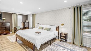 Quarto com cama grande, cabeceira de madeira, mesas de cabeceira, cômoda e uma janela com cortinas.