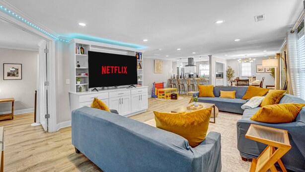 Uma sala de estar moderna com uma TV de tela plana exibindo 'NETFLIX', um sofá e uma área de jantar com mesa e cadeiras.