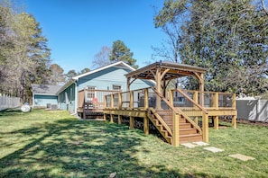 A backyard with a wooden deck, a covered play area, and a house in the background. - The Grand Ranch: 6-BR Luxury Retreat with with Gazebo, Fire Pit & Outdoor Cinema (Raleigh)