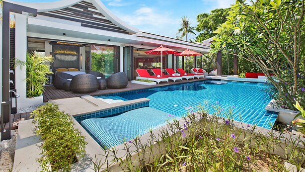 Un espace moderne aménagé au bord de la piscine, avec des chaises longues et des parasols, une piscine et une végétation luxuriante.