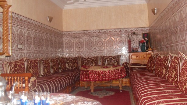 A traditional Moroccan room with patterned tile walls, a chandelier, a sofa set, and a small table with a red tablecloth.