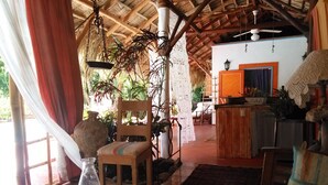 Une pièce chaleureuse avec un plafond en bois, une table à manger agrémentée d’un vase et d’une bougie, une chaise, et une vue sur un coin cuisine.
