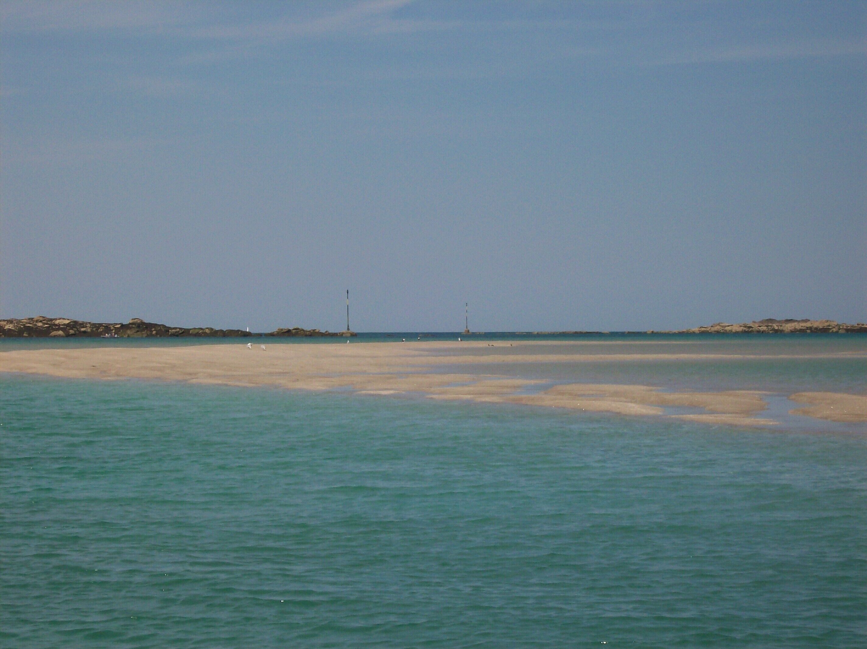 A beach with calm waters and a distant rocky shoreline.