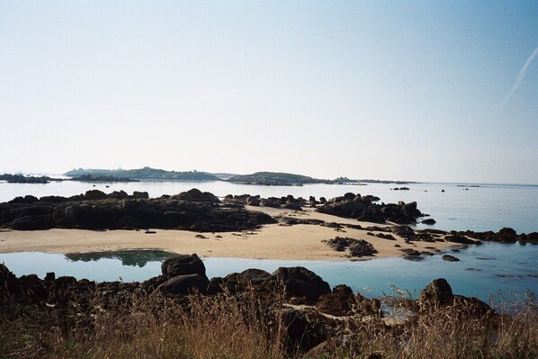 A coastal landscape with rocky outcrops, a sandy beach, and calm water.