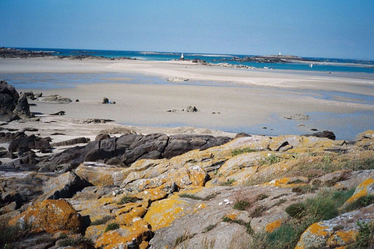 A rocky shoreline with a sandy beach and a lighthouse in the distance.