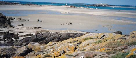 A rocky shoreline with a sandy beach and a lighthouse in the distance.