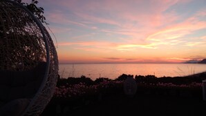 Vista del atardecer desde un balcón con una silla de mimbre y una lámpara colgante.