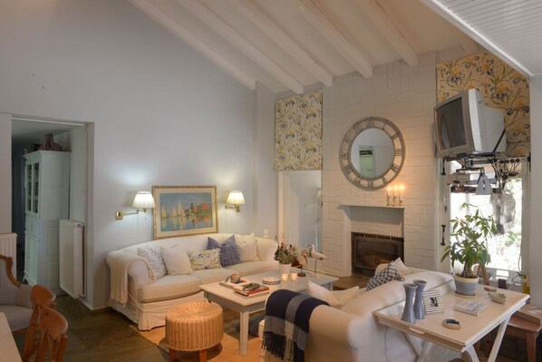 A cozy living room with a white sofa, a coffee table, a fireplace, and a television.